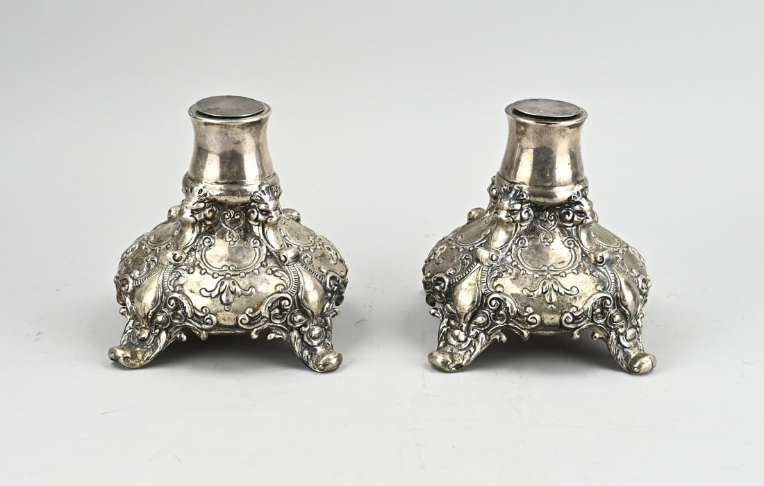 2 Silver pedestals: Two silver pedestals, 835/000, square contoured model decorated with garlands, volutes and floral decoration. Placed on 4 curled legs. 16x16x17cm. Total approx. 2075 grams. In good condition.