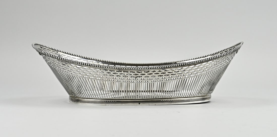 Silver basket: Silver boat-shaped bread basket, 833/000, openwork basket with bars and oval decoration. The basket has a pearl rim and is placed on an oval ring with filet rim. 33x18.5x9cm. MT.: DAMeijer, Leiden,