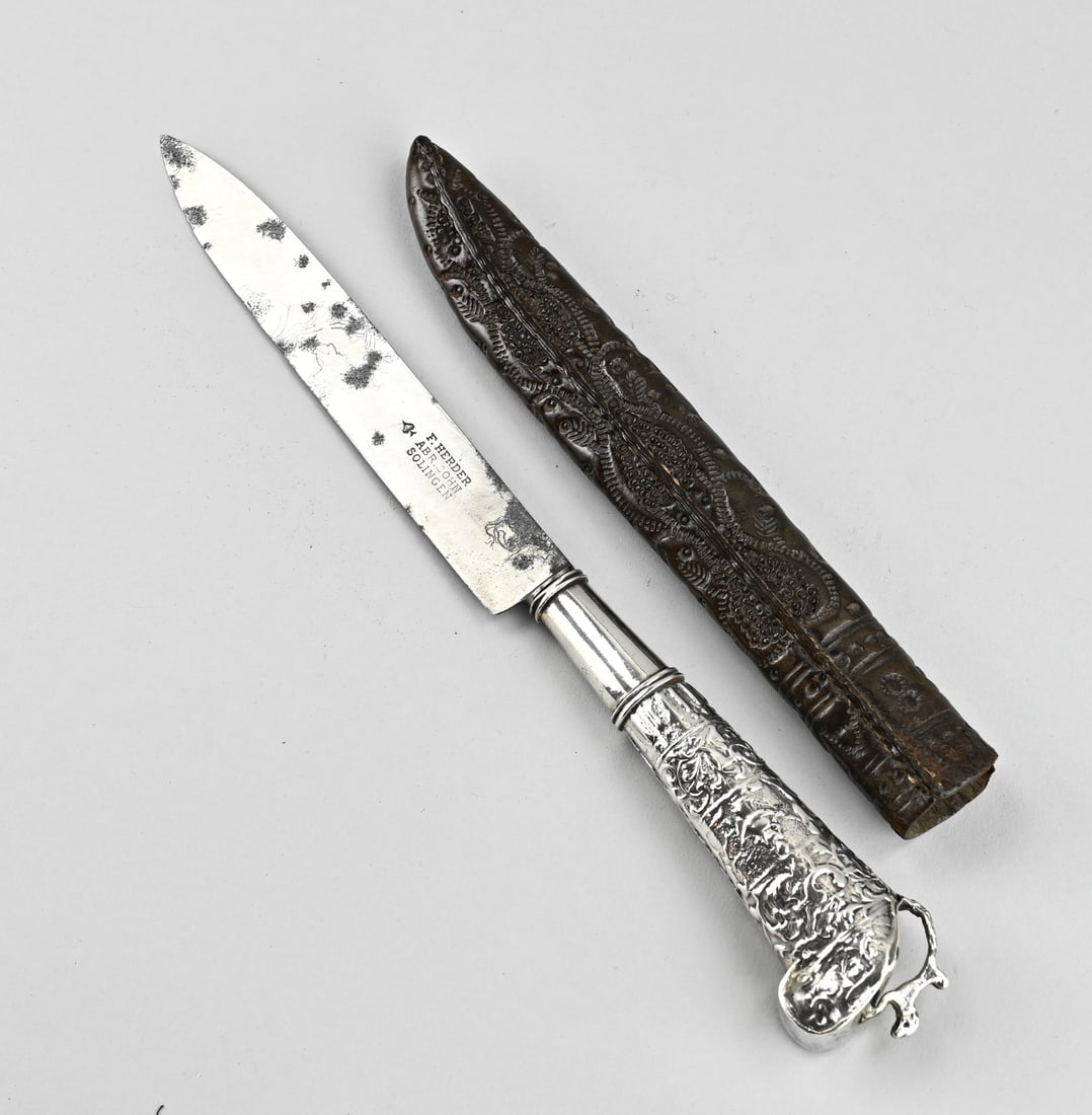 Travel knife with silver in sheath: Travel knife in leather sheath with a silver handle in the shape of a pistol decorated with bandelwork with figures. Crowned with a dog. Length 28 cm. In good condition.