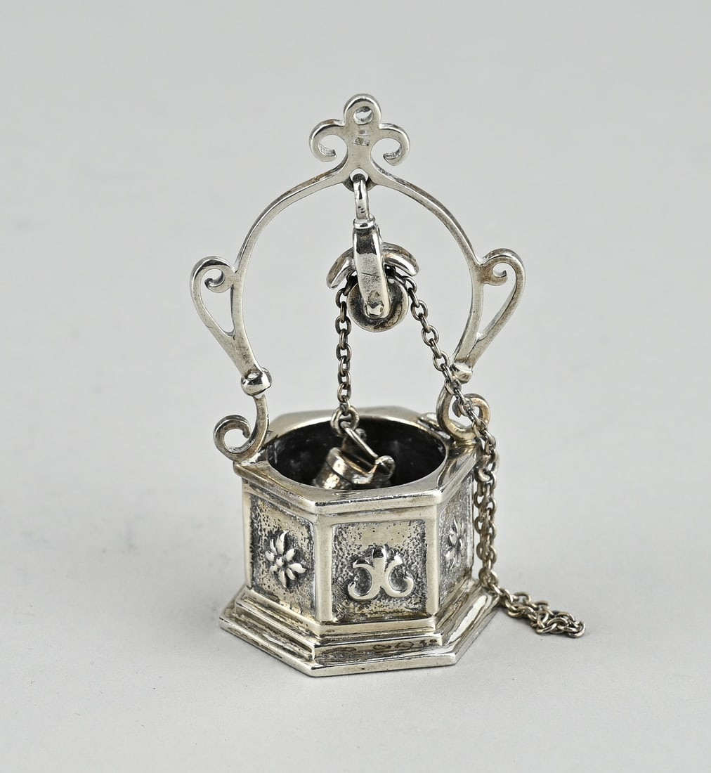 Silver miniature water well: Silver water well, 835/000, hexagonal with floral decoration and a bucket on a chain with pulley. MT.: Amsterdam Diamond Company. Amsterdam, after 1965. 4x3x7cm. approx. 50 grams. In good condition.