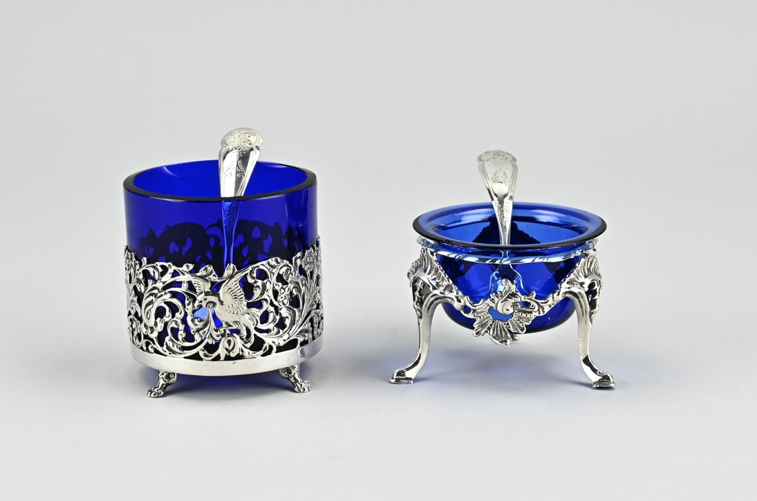2 Silver salt cellars with spoons: Lot with 2 silver salt cellars with blue glass and a silver holder. A cylindrical salt cellar with a silver holder with Biedermeier work on 4 claw feet. With a blue glass inner bowl. MT.: Fa. Dahlia,