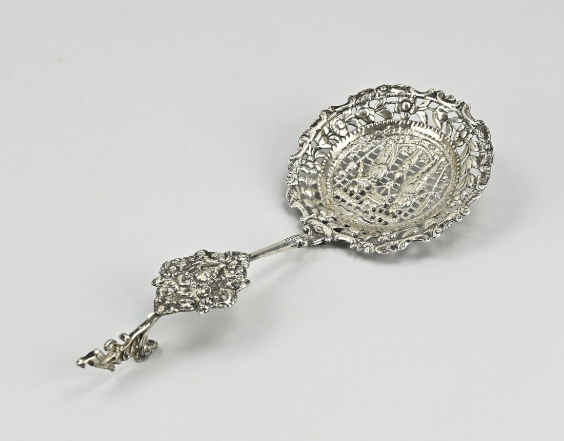 Silver wet fruit scoop: Silver wet fruit scoop, 833/000, with a round sawn bowl with figures and a floral edge. The curved handle has a silver element with putti and crowned with an eagle. 21x8cm. approx. 76 grams.