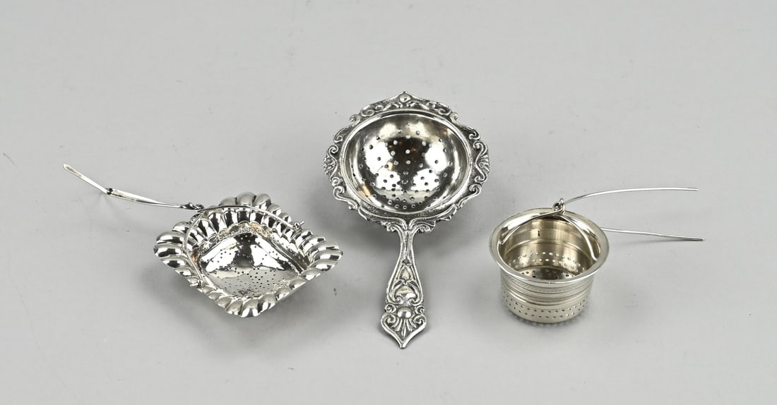 3 Silver tea strainers: Lot with 3 silver tea strainers, 833/000, with a cylindrical model with band work, ø 37.5 mm., a rectangular contoured model with lobed work, 6x4.5cm. and a round contoured model with stem. The edge
