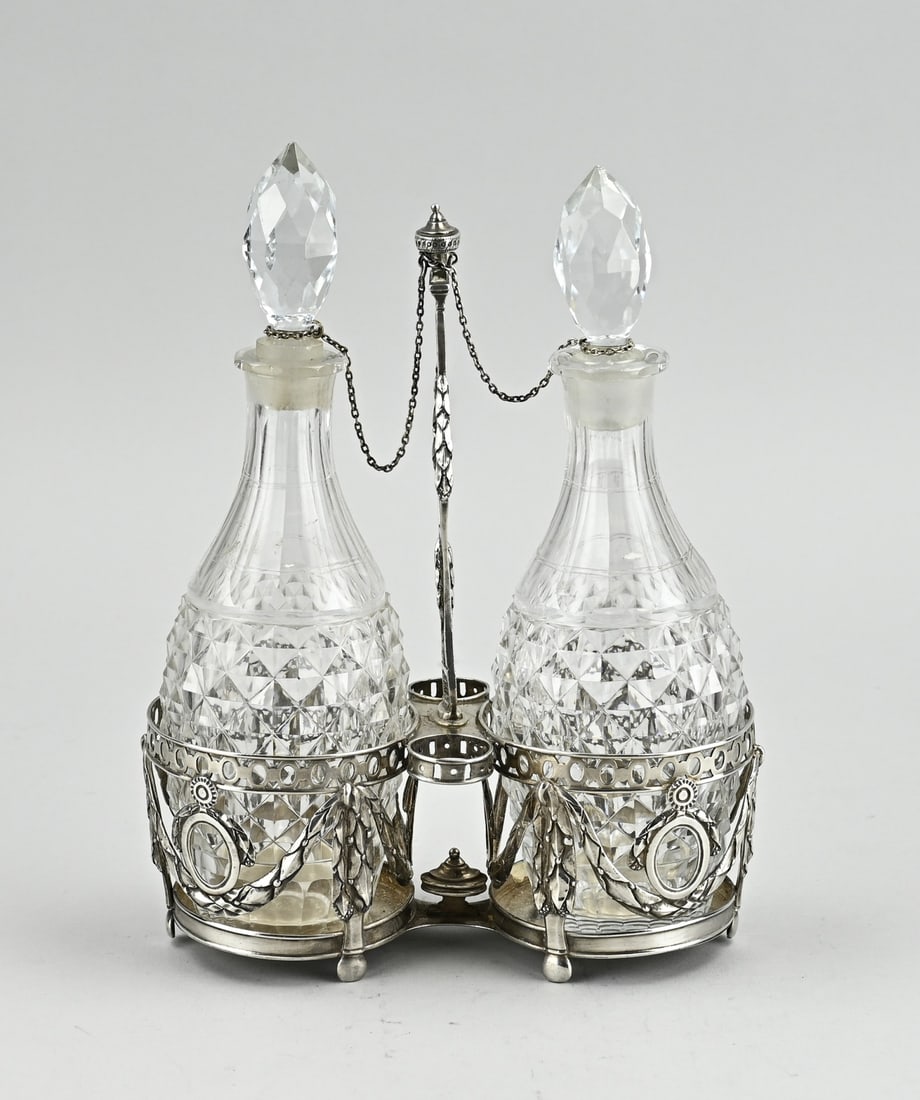Oil and vinegar set: Crystal oil and vinegar set in a silver holder, 18th century. 2 Cylindrical holders decorated with garlands, medallions and floral decoration. Provided with a handle with a crown and floral