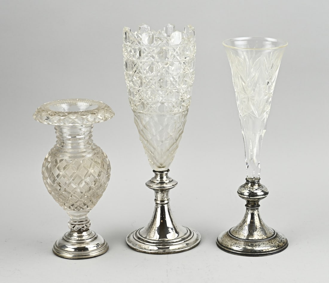 3 Crystal vases on silver base: Three crystal vases on silver base, 835/000. Low vase with grinding and a folded edge, placed on a silver base with pearl edges, slightly out of shape. ø12.5x23cm. a vase with star-shaped grinding,