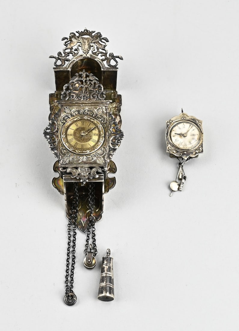 2 Silver miniature clocks: Two silver miniature clocks, 835/000, with a Zaanse clock with vases and a chain with pulley and weight. 19 cm. And a small hanging clock with pendulum and weights. 6 cm. Both clocks are placed on a