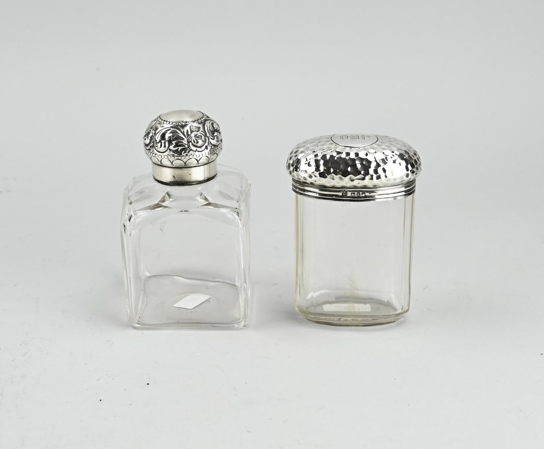 2 Bottles with silverware: Two crystal bottles with silver, 925/000. An oval bottle with a hammered finish on the lid. Provided with a monogram engraving: OMP. MT.: Drew & Sons, London, jl.:g:1902. 7x4.5x10.5cm. And a