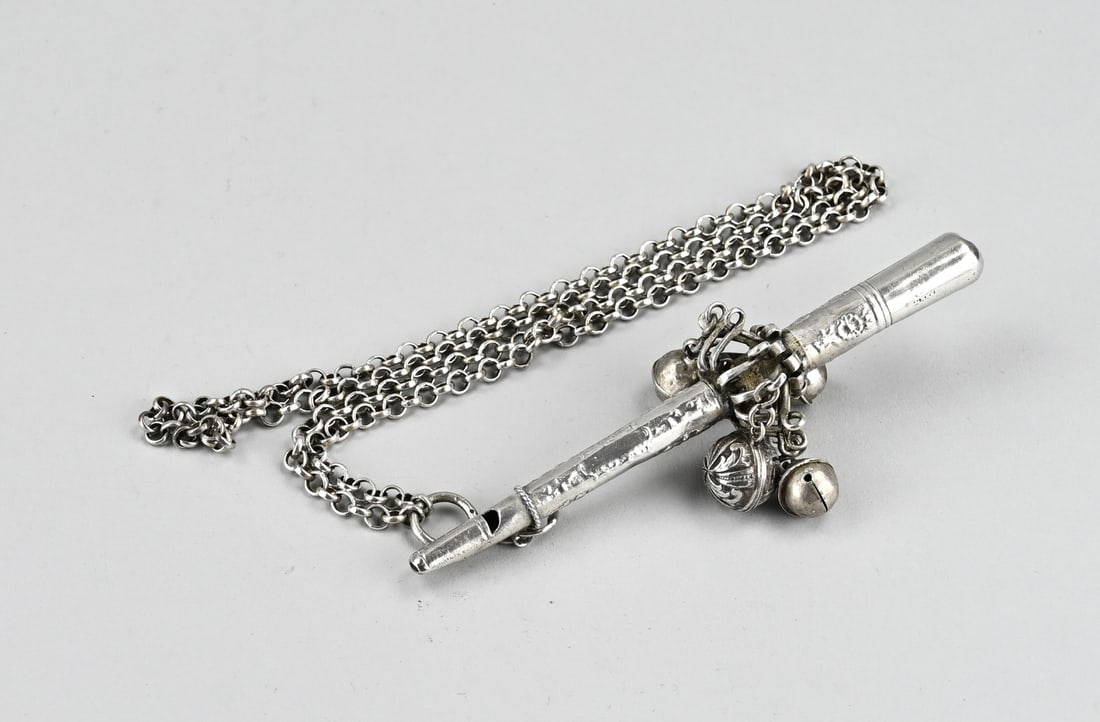 Silver rattle on chain with whistle/bells: Silver rod rattle, 18th century, with a whistle and 4 bells. The rattle has a silver jasseron chain. approx. 76 grams. length 14 cm. length chain approx. 80 cm. Somewhat dented and worn, otherwise in
