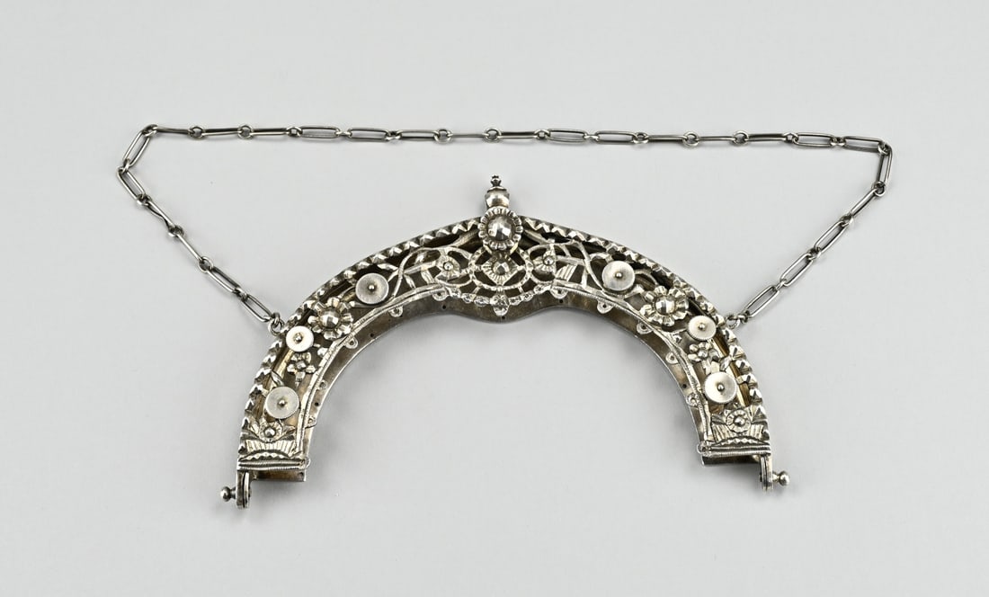 Silver bag bracket: Large silver purse clasp, 833/000, round openwork model decorated with coins. MT.: Unclear, Schoonhoven. The clasp is provided with a chain. approx. 230 grams. Width 18 cm. In good condition.