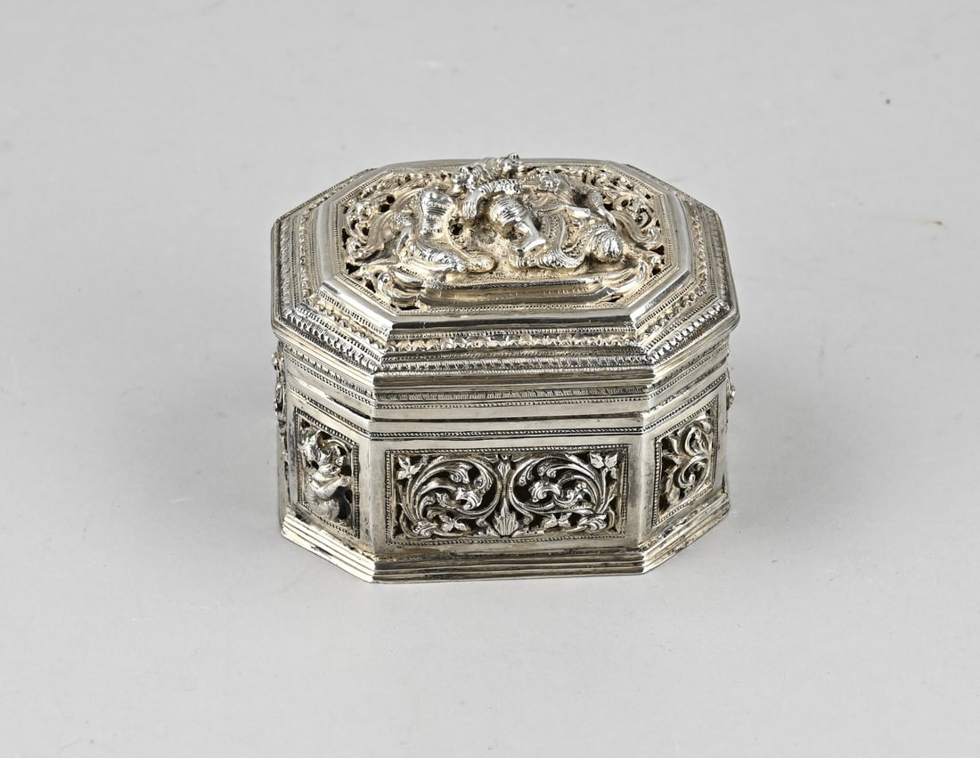 Silver box Burma: Silver box, rectangular contoured model decorated with curls, volutes and animal figures. On the openwork lid is a representation with 2 figures. Burma. 11x9x8cm. approx. 260 grams. In good condition.