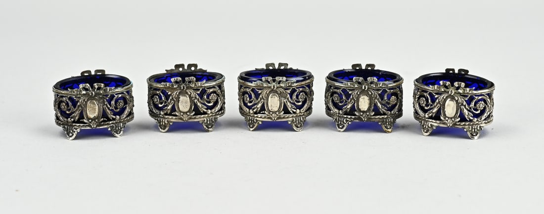 Cassette with 5 silver salt cellars: Case with 5 silver salt cellars with blue glass. Oval silver holders decorated with garlands, bows and medallions. 3,8x2,6x2,5cm.