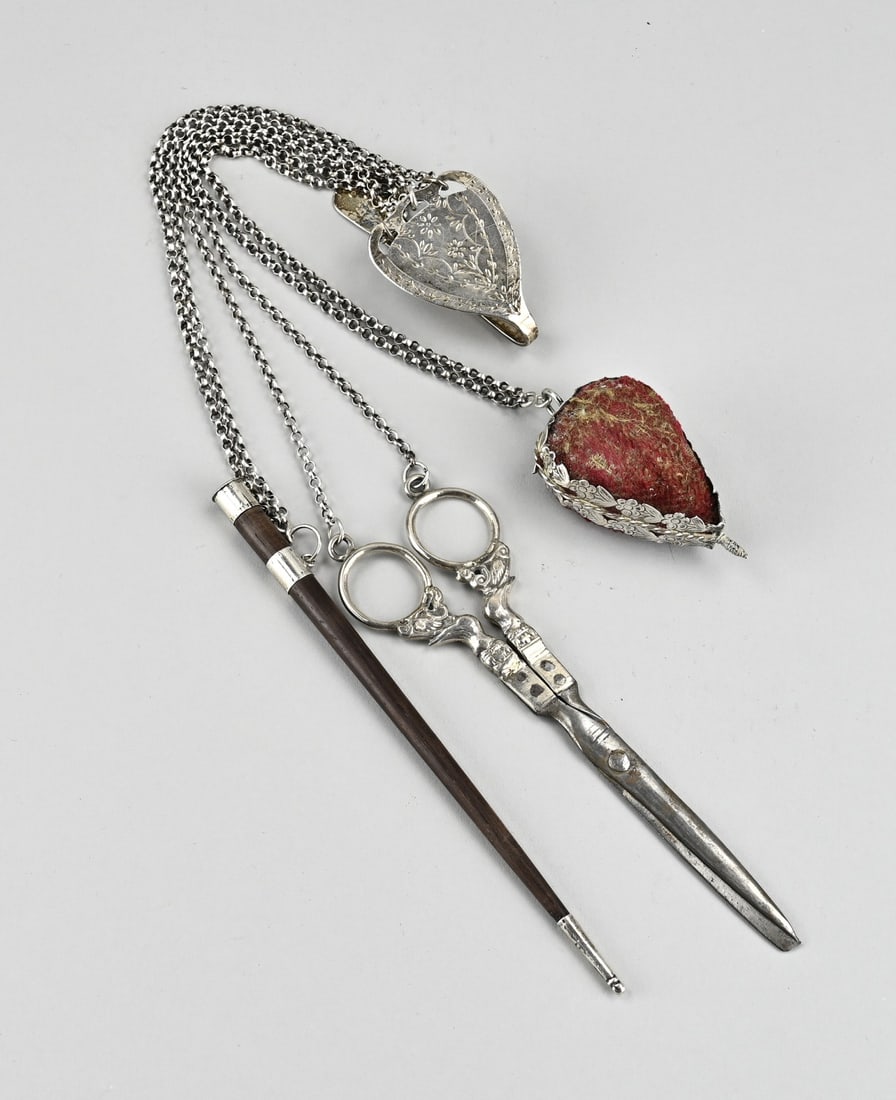 Chatelain with skirt hook, scissors, knitting sheath etc.: Silver skirt hook with a chatelaine with a heart-shaped pincushion, a pair of scissors with silver handles and a wooden knitting sheath with silver. 833/000. 47 cm. approx. 166 grams. In good