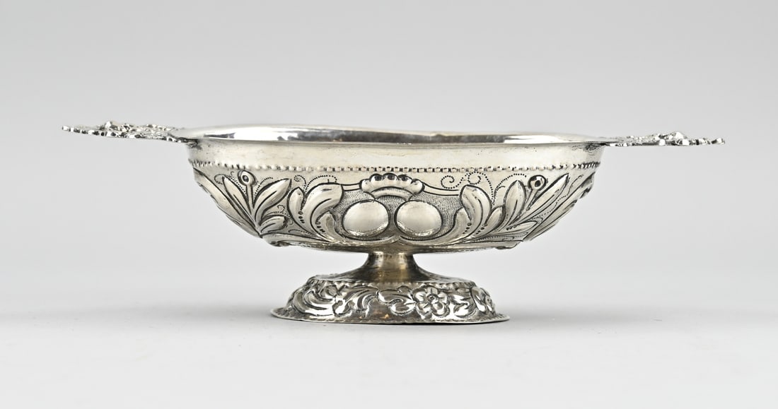 Silver brandy bowl: Antique silver brandy bowl, with embossed decoration with floral decoration and grid decoration. With 2 horizontally placed handles with putti. Size: Probably Johannes Andringa Leeuwarden, 1756.