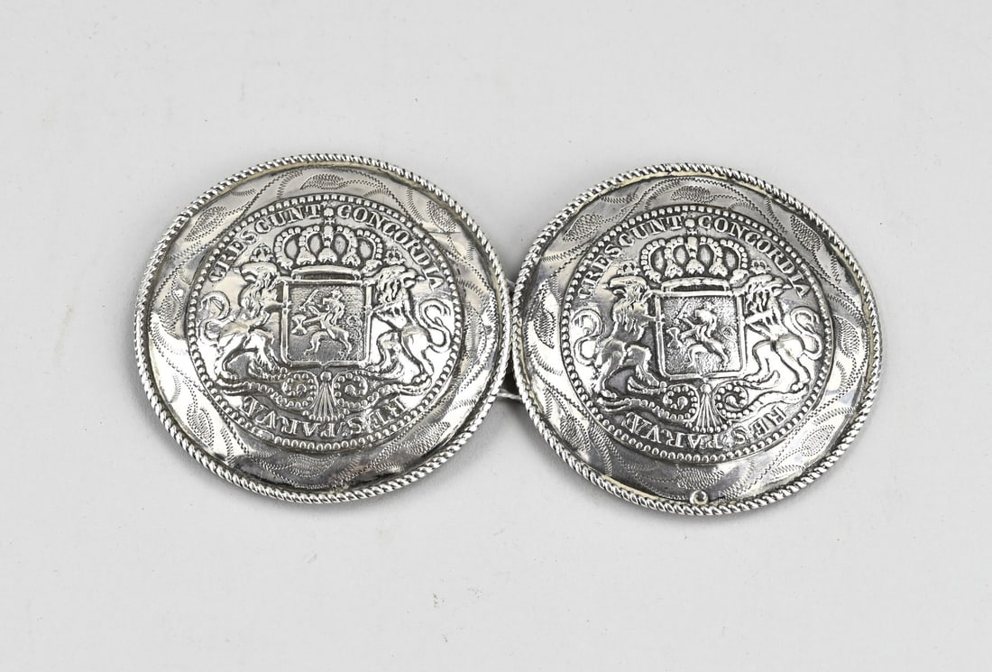 Silver trouser pieces: Two silver trouser pieces, 833/000, round with an image of the national coat of arms with lions and a crown. Schoonhoven, approx. 92 grams. ø 8.5cm. Connected by means of a silver bracket.