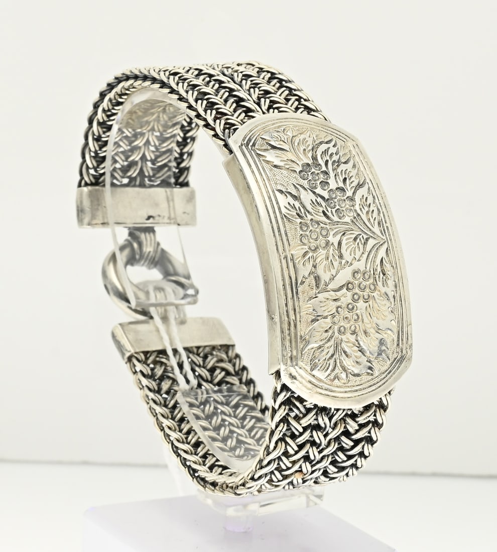 Silver bracelet: Silver wide bracelet, 925/000, with floral centerpiece. Bracelet with 2 rows of braided links with an oval element in the middle decorated with floral decoration. The bracelet has a spring eye.