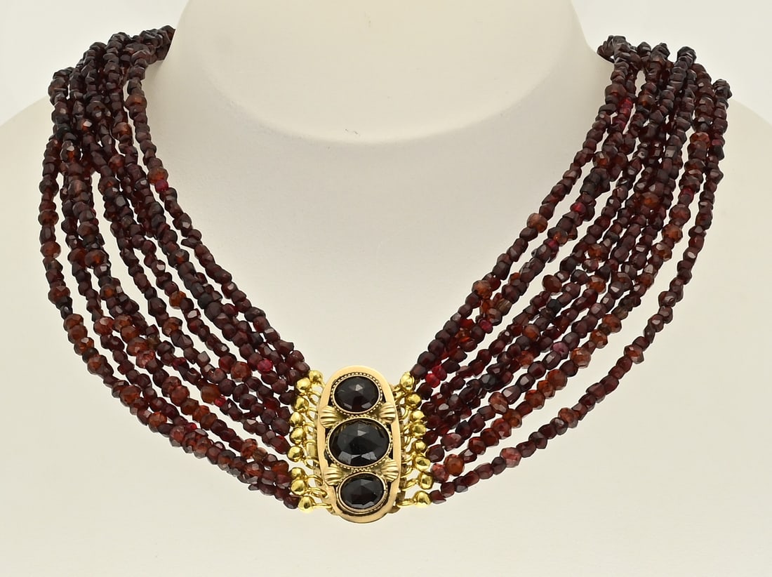 Garnet necklace with gold clasp: Necklace with garnet beads and yellow gold clasp, 750/000. Necklace with 9 strings of faceted garnet beads, ø 3 mm. The strings are attached to an oval clasp set with 3 oval faceted garnet beads.
