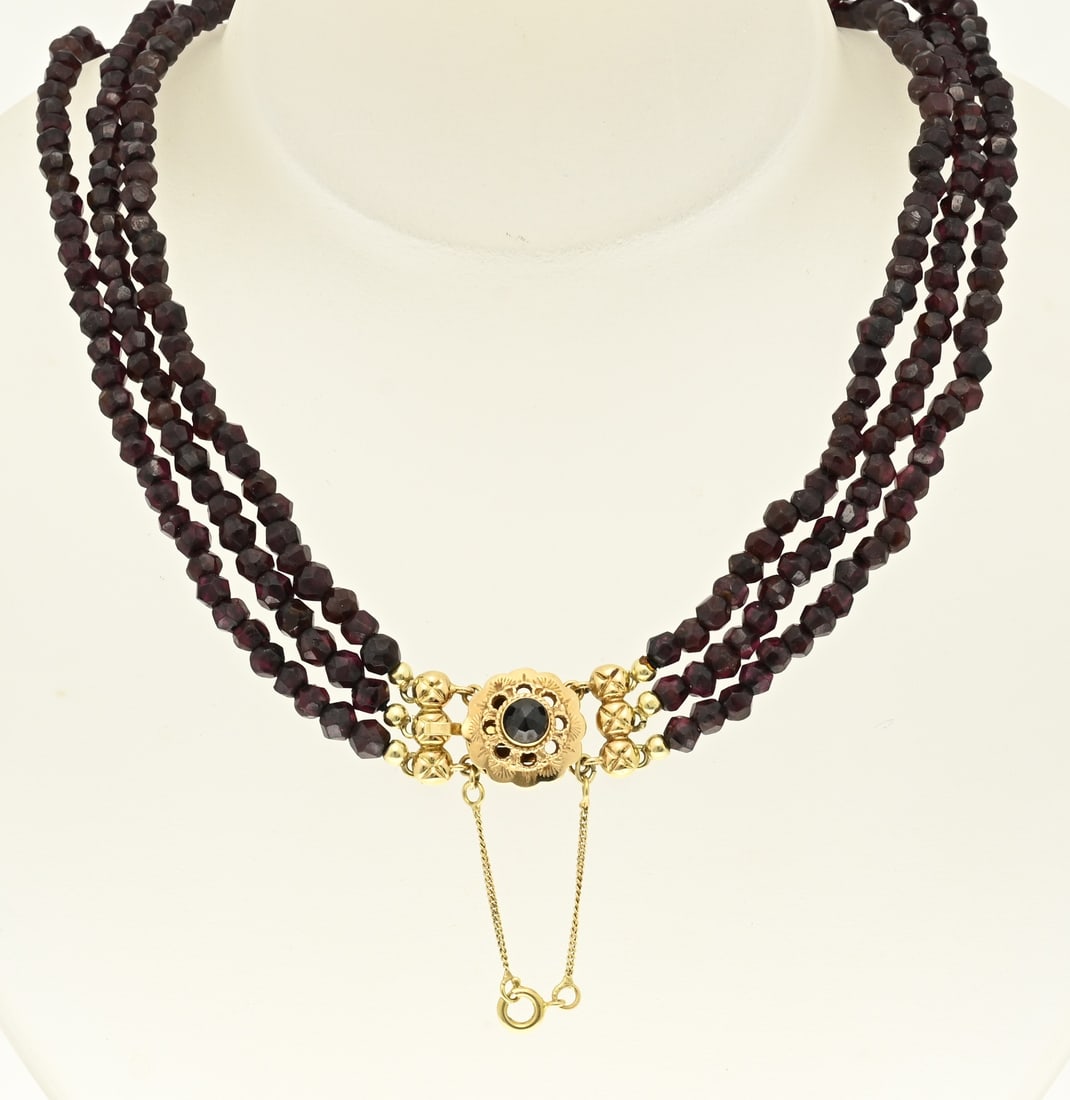 Garnet necklace: Necklace of 3 rows of faceted garnet beads, ø 4.5 mm., attached to a yellow gold clasp, 585/000, in a flower shape with yellow gold end pieces and a safety. Length 38 cm. approx. 48 grams. In very