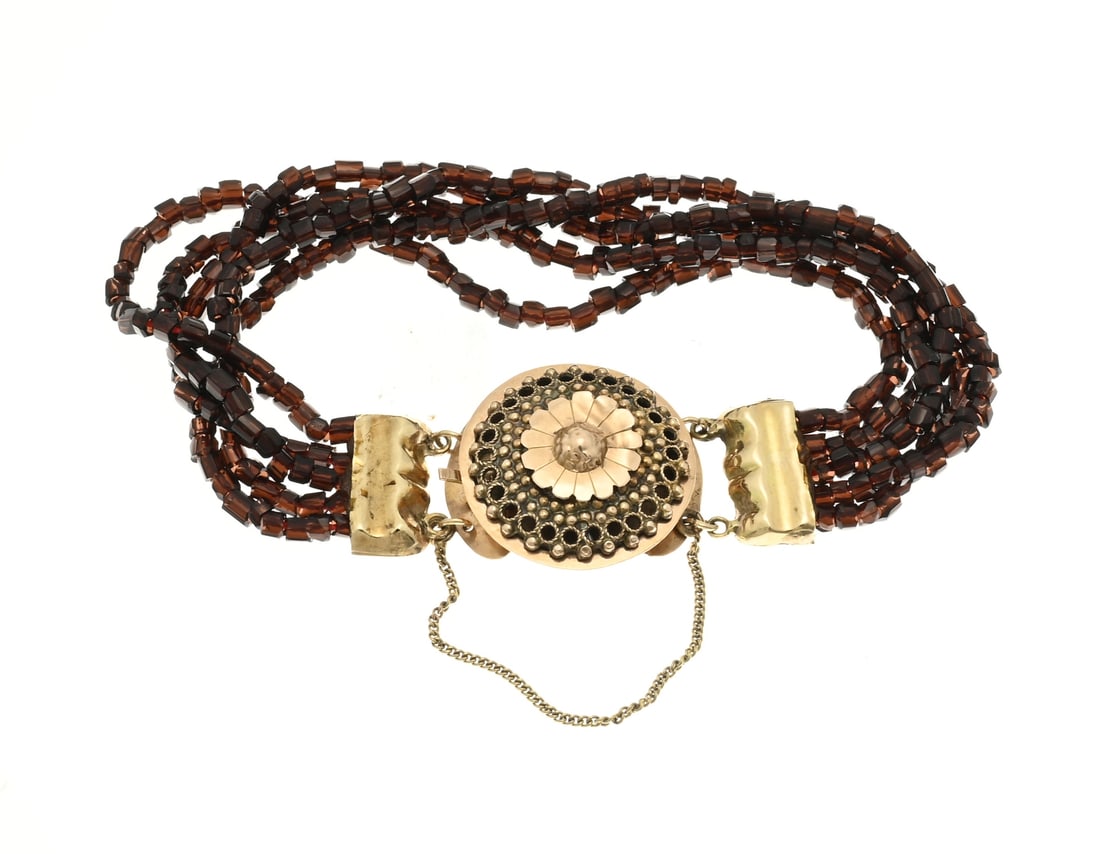 Bracelet with garnet and gold clasp: Bracelet with 5 rows of cylindrical cut garnet stones with large yellow gold clasp, round model with filigree work with soldered flower-shaped element. ø clasp 23.5 mm. The bracelet has rectangular