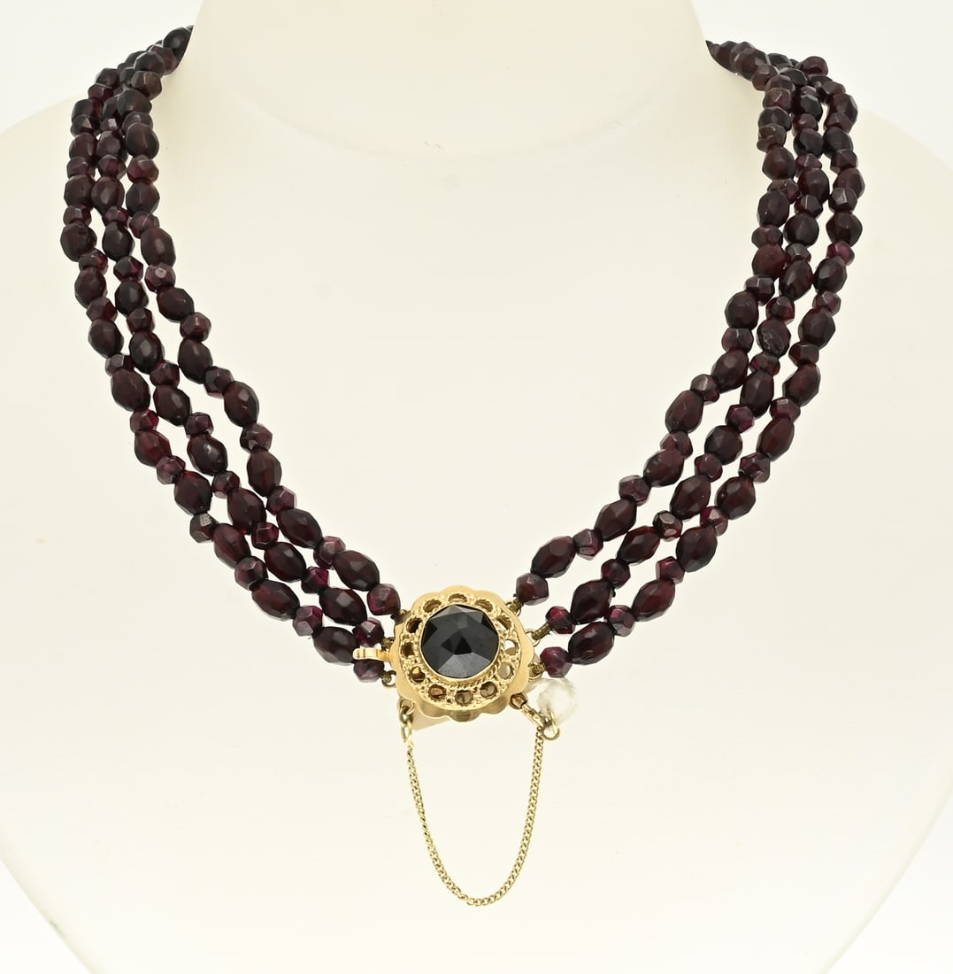 Necklace of 3 rows of garnet and gold clasp: Necklace of faceted garnet beads, round and oval, attached to a round yellow gold clasp, 585/000, with a scalloped edge, filigree edge and garnet stone. The necklace is provided with a safety. length