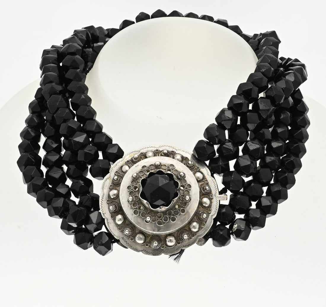 Necklace of jet with silver clasp: Necklace of 4 rows of cut jet beads, ø 9 mm, attached to a large round regional clasp with balls and buttons. In the middle of the clasp is a jet bead. length 37 cm. 5th row incomplete. approx. 183