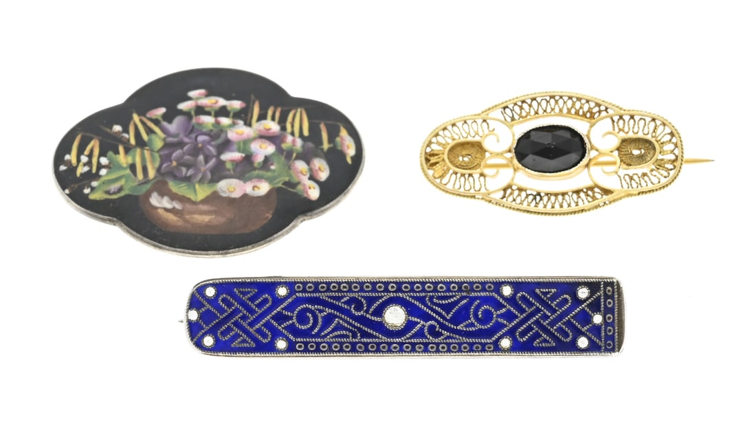 Lot with 3 silver brooches: Lot with 3 brooches, an oval contoured model with filigree provided with a jet stone, a rod-shaped brooch with blue and white enamel and an oval contoured brooch with a painting of a flower basket.