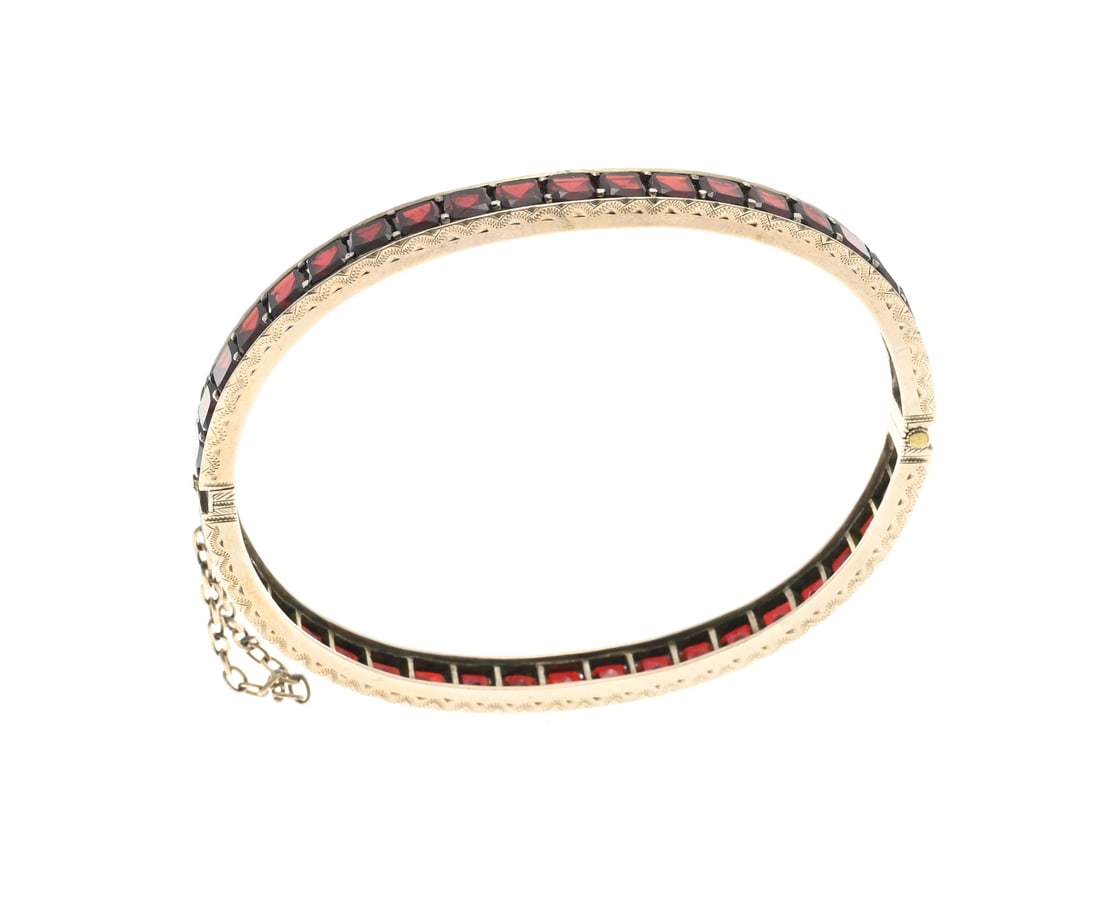 Bangle with garnet, row: Bangle with a row of garnets, silver plated, set all around with square faceted garnets. Fitted with a hinge and box clasp. And a safety chain. width 5 mm. 58x48 mm. 12.8 grams. In good condition.