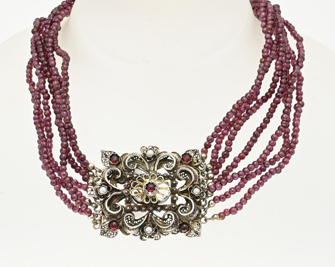 Necklace with garnet and silver clasp: Necklace with 7 rows of round faceted garnet beads, ø 3 mm., in the middle attached to a large square silver clasp decorated with garnet stones and pearls. width 37 mm. length 38 cm. approx. 59