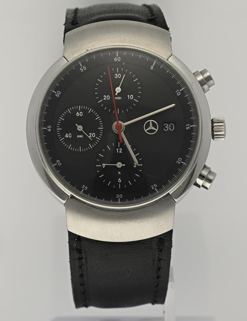 Mercedes watch: Mercedes Benz design watch, with a steel case. Chronograph, black dial and date display. Automatic. Equipped with a glass back cover. ø 40 mm. With black leather strap. Glass is slightly scratched.