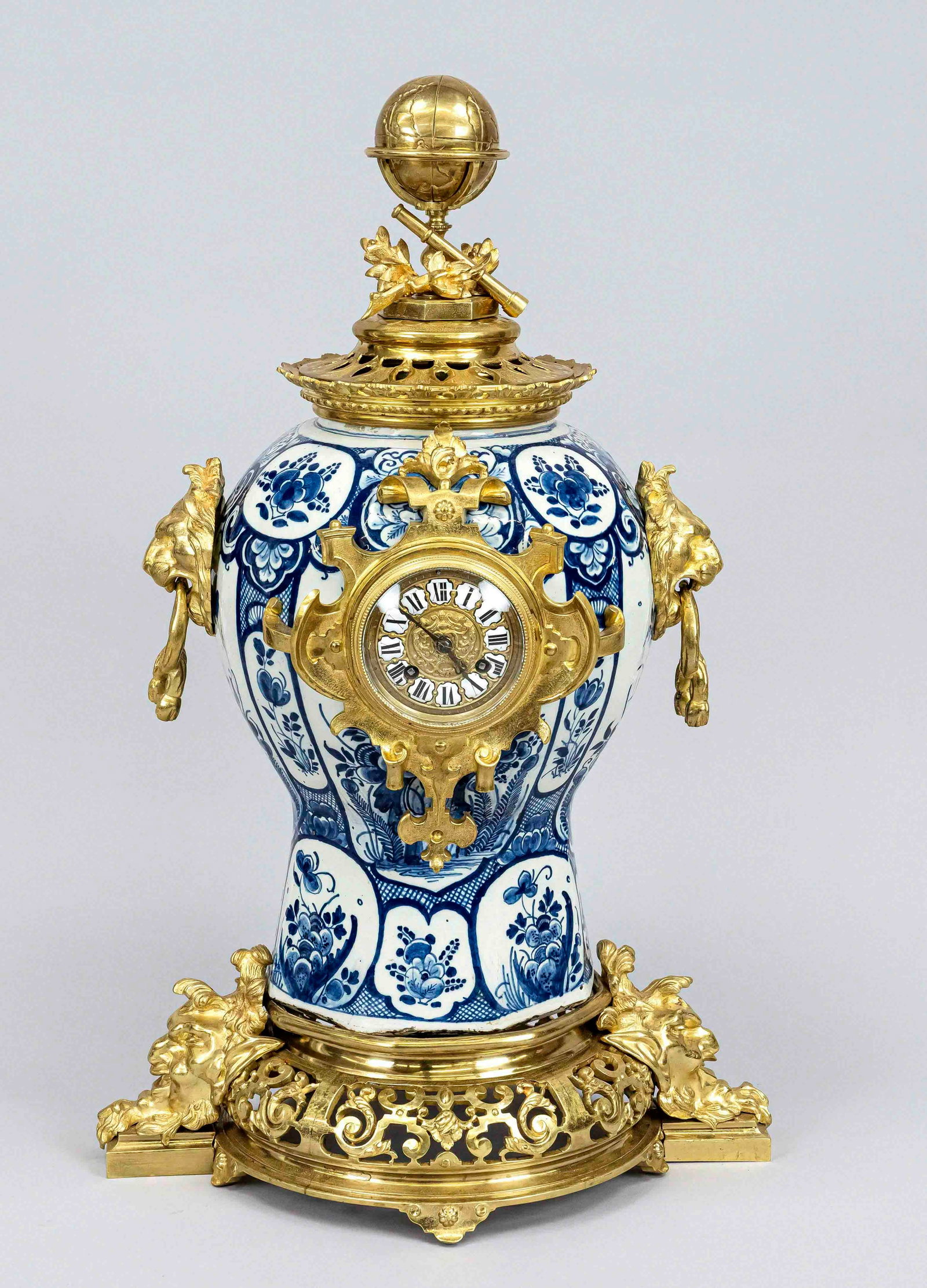Pendulum, Delft with bronze: Large Delft faience mantel clock with gilded bronze mounts. With lions + faun heads + globe on top. Circa 1880. Eight-day movement, half-hourly striking, spring pendulum. Dimensions: H 65 cm. In good