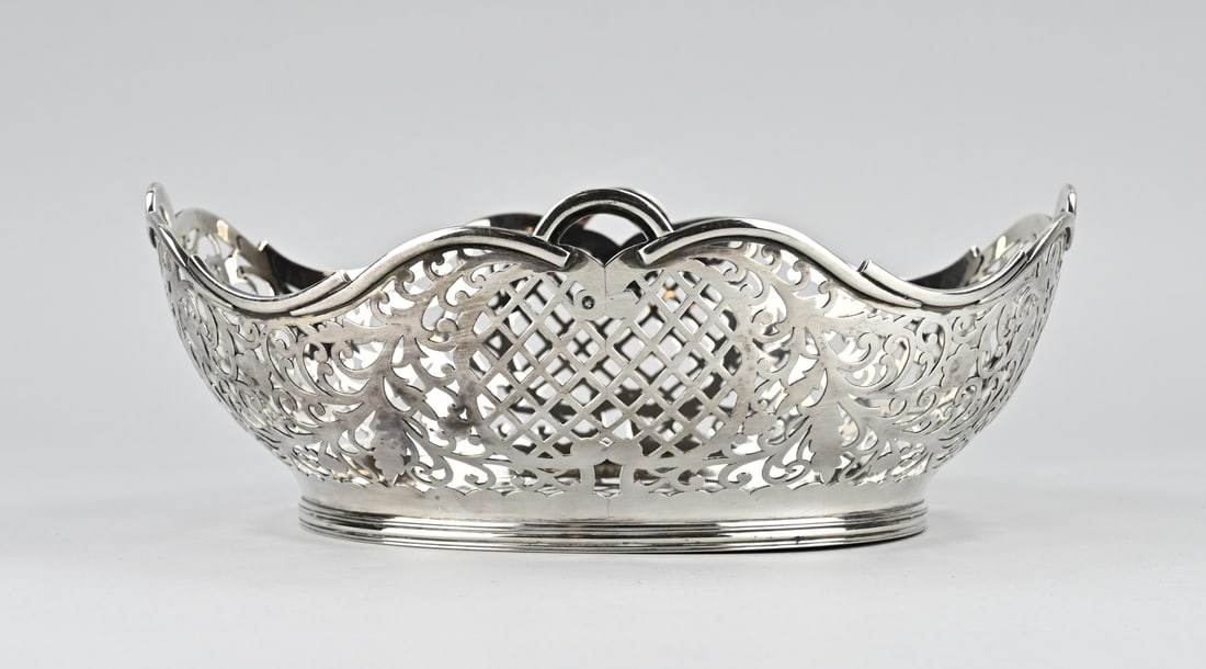 Silver bread basket: Silver bread basket, 934/000, oval sawn model with grid, curls and floral pattern. with a soldered edge of volutes. And placed on an oval ring with filet edge. MT.: Fa. Hoogsteiling & Presburg,