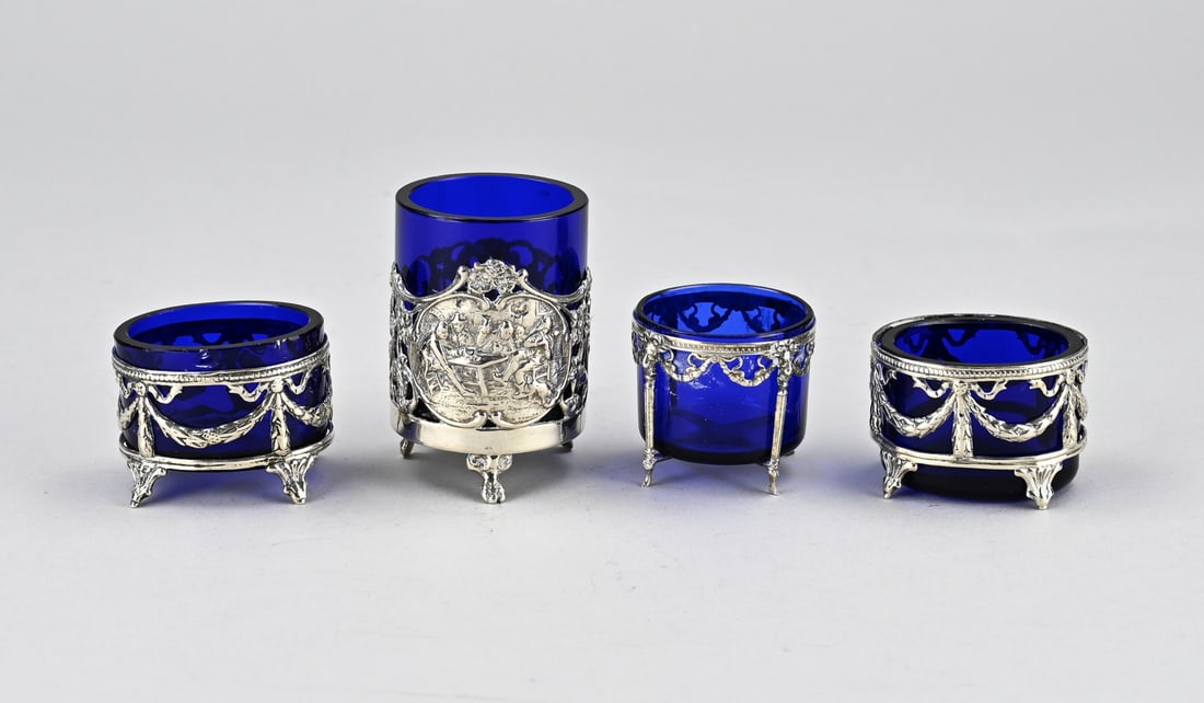 4 Silver holders, with 3 salt cellars and mustard pot: Four silver holders with blue glass. 2 Oval silver holders, 800/000, with garlands and culot-shaped feet. 5x4x3.5cm. 2 Round holders, 833/000, one with Biedermeier decor and representations, on claw