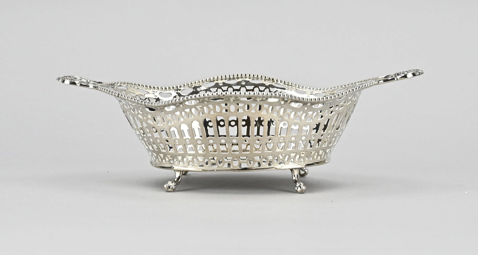Silver candy basket: Silver bonbon basket, 833/000, oval contoured model with sawn bars and oval decoration. The basket has a pearl rim and handles with floral decoration. The basket is placed on 4 claw feet. 20x12x6cm.