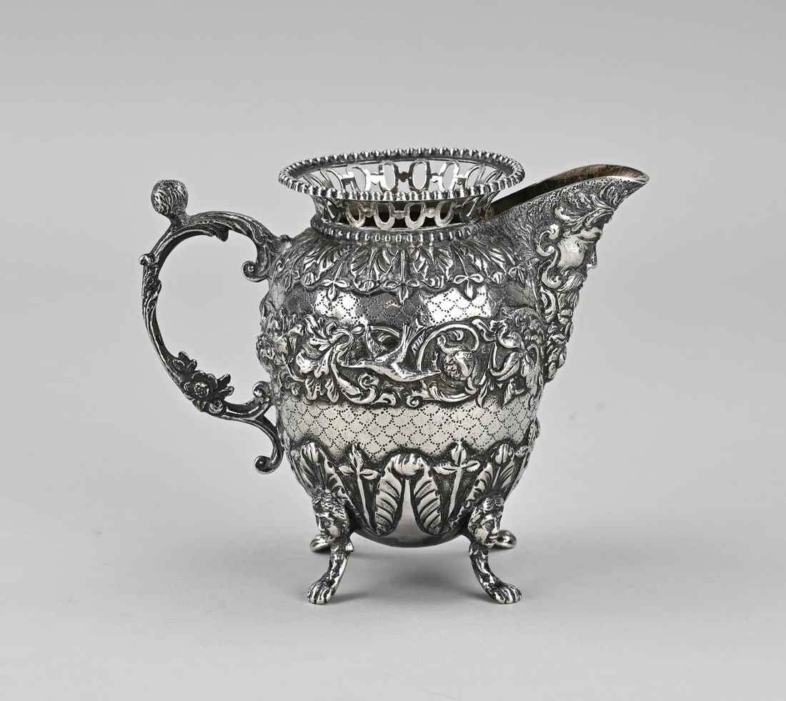Silver milk jug: Silver milk jug, 833/000, richly decorated with acanthus leaves, floral and animal decoration. With an image of a face in the spout and a curled handle with flower and head. Placed on 4 claw feet and