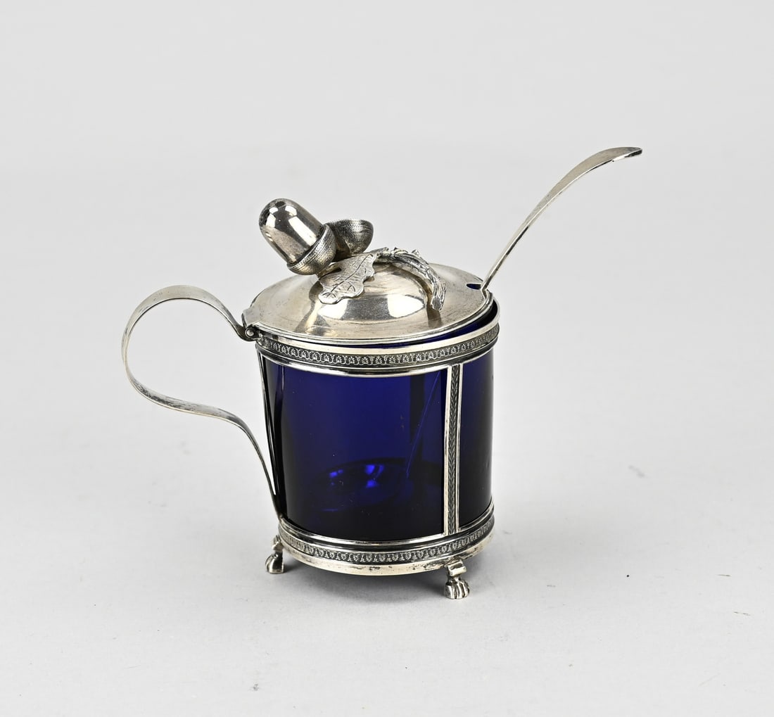 Silver mustard pot: Mustard pot with silver holder and spoon, 833/000, with blue glass inner container. Cylindrical holder on 3 claw feet with bands decorated with palmettes. The hinged lid is provided with a loose