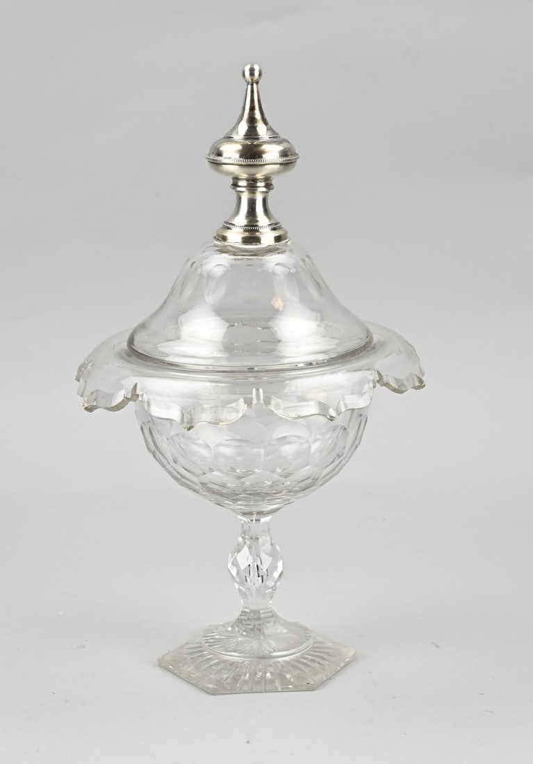 Candy cup with silver knob: Crystal candy cup on hexagonal base and provided with a folded edge with aculade shape. Provided with a lid with silver knob with pearl edge. Minimal chips. In good condition. ø18x33cm.