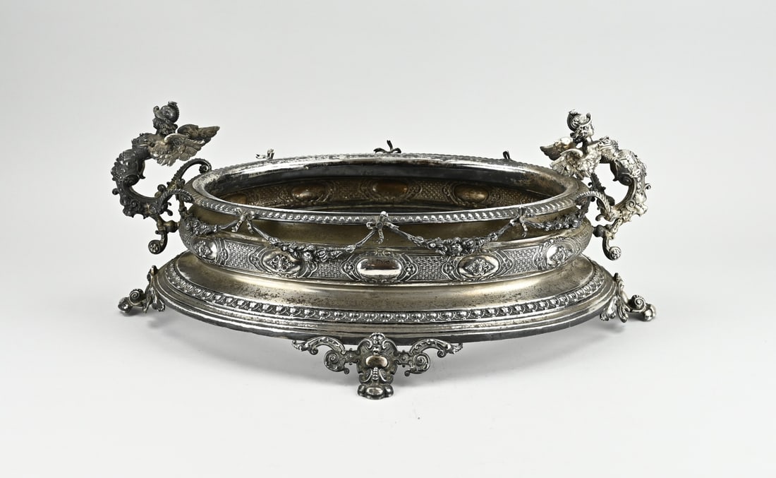 Silver centerpiece: Large silver centerpiece, 800/000, oval model richly decorated with bows, garlands, cartouches and a knerren rim. The centerpiece has 2 handles in the shape of a winged mermaid. The piece is placed on