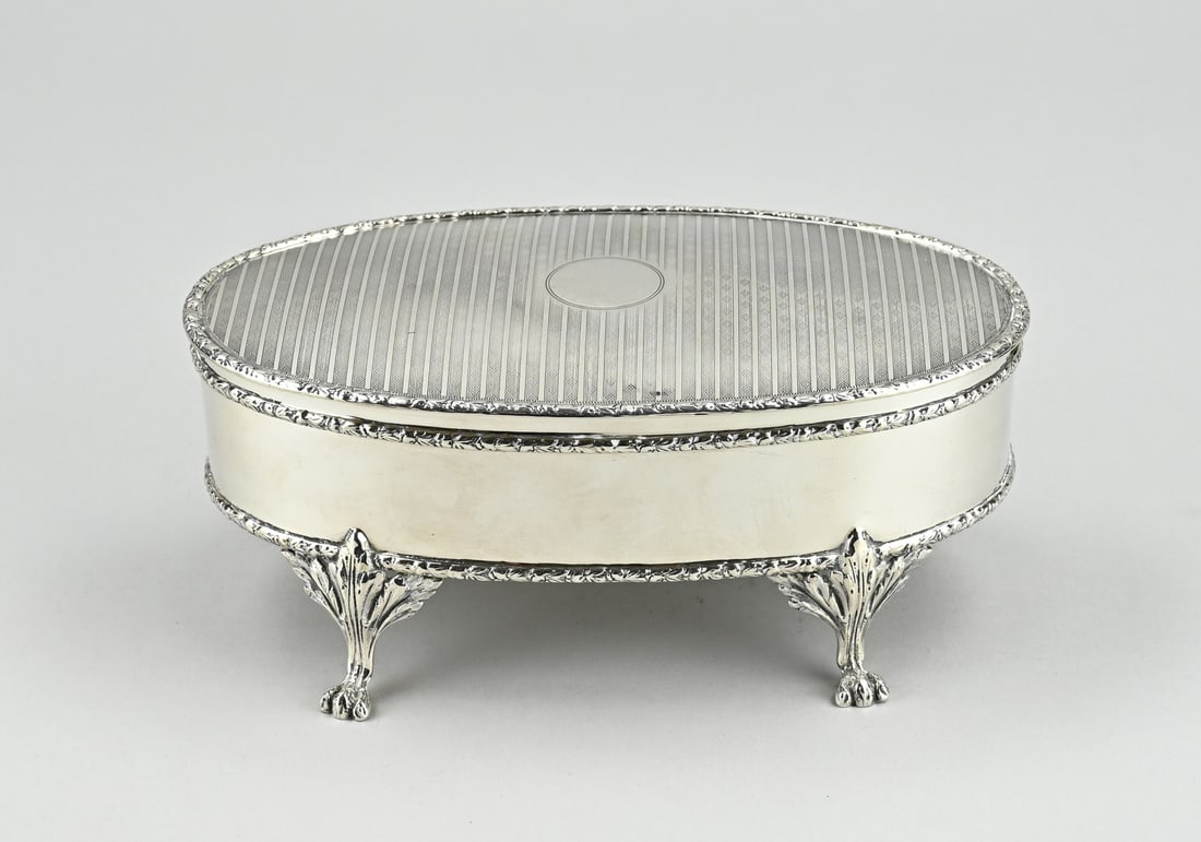 Silver box, oval: Silver box, oval model richly decorated with driven volutes and flowers and embellished with engraving. The box is placed on claw feet. And the lid is provided with soldered floral elements. Probably