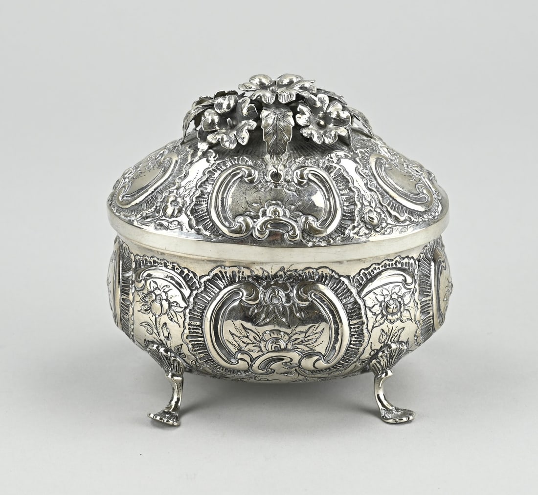 Silver lidded box, oval on 4 legs: Silver box, oval model richly decorated with driven volutes and flowers and embellished with engraving. The box is placed on claw feet. And the lid is provided with soldered floral elements. Probably