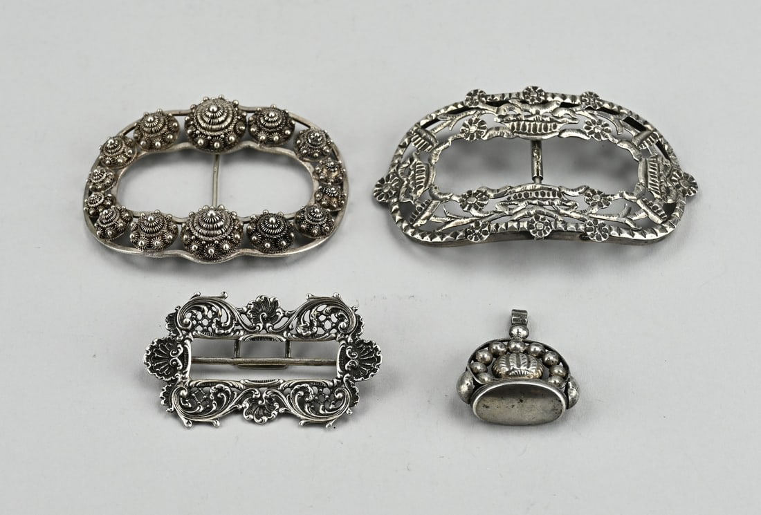 3 Silver buckles and a cachet: Three silver buckles and a cachet. A rectangular model, 800/000, with floral decoration, 7x4cm., An oval buckle decorated with Zeeland buttons, 833/000, 8.3x6.5cm., and an oval buckle, 833/000, sawn