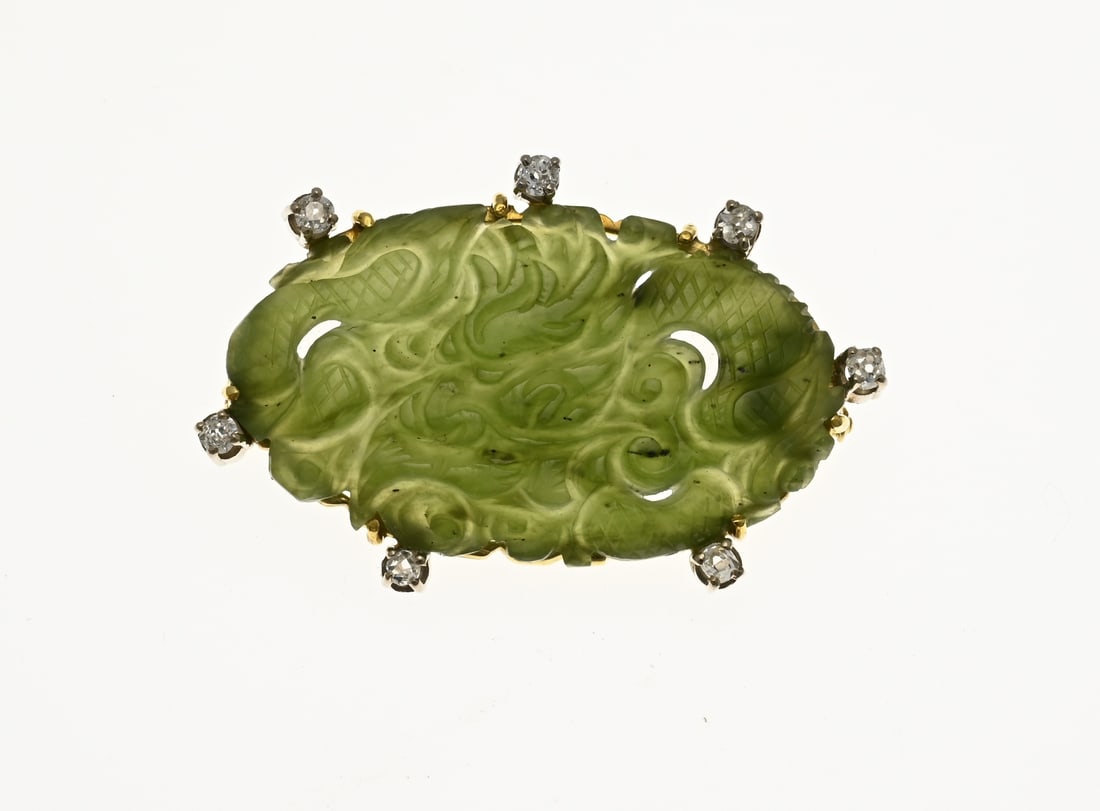 Gold brooch with carved jade stone: Yellow gold brooch, 585/000, with jade and diamond. Oval brooch set with an oval cut jade stone. The gold setting edge is decorated with 7 white gold chatons set with diamonds with an old brilliant