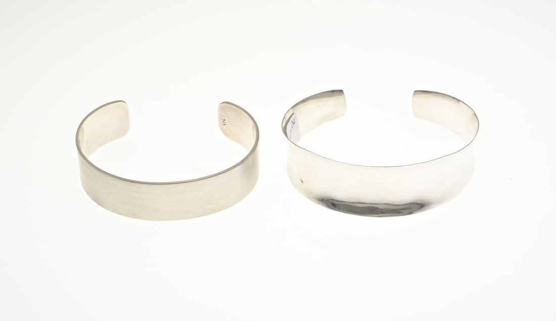 2 Silver bangles: Two silver bangles, 925/000, a flat matt clamp band, width 17 mm. and a concave clamp band, tapering in width. Width 12-21 mm. Both new. approx. 47 grams.