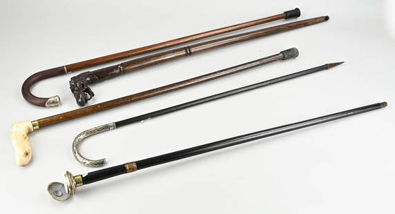 Walking sticks in holder (5x): Five various old/antique walking sticks in holder, one with silver handle. 20th century. Size: 85 - 90 cm. In good condition.