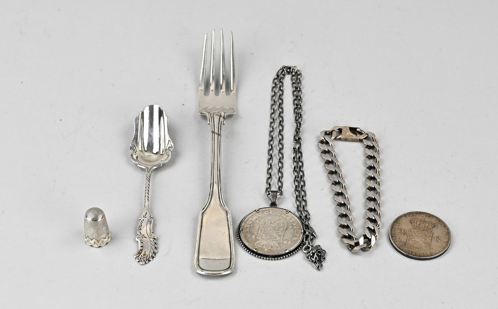 Lot of various silver, 6x: Lot of 6 silver pieces, including a table fork, a sugar spoon, a thimble, a bracelet, a necklace, and two coins. Various grades. Total approximately 182 grams. In good condition.