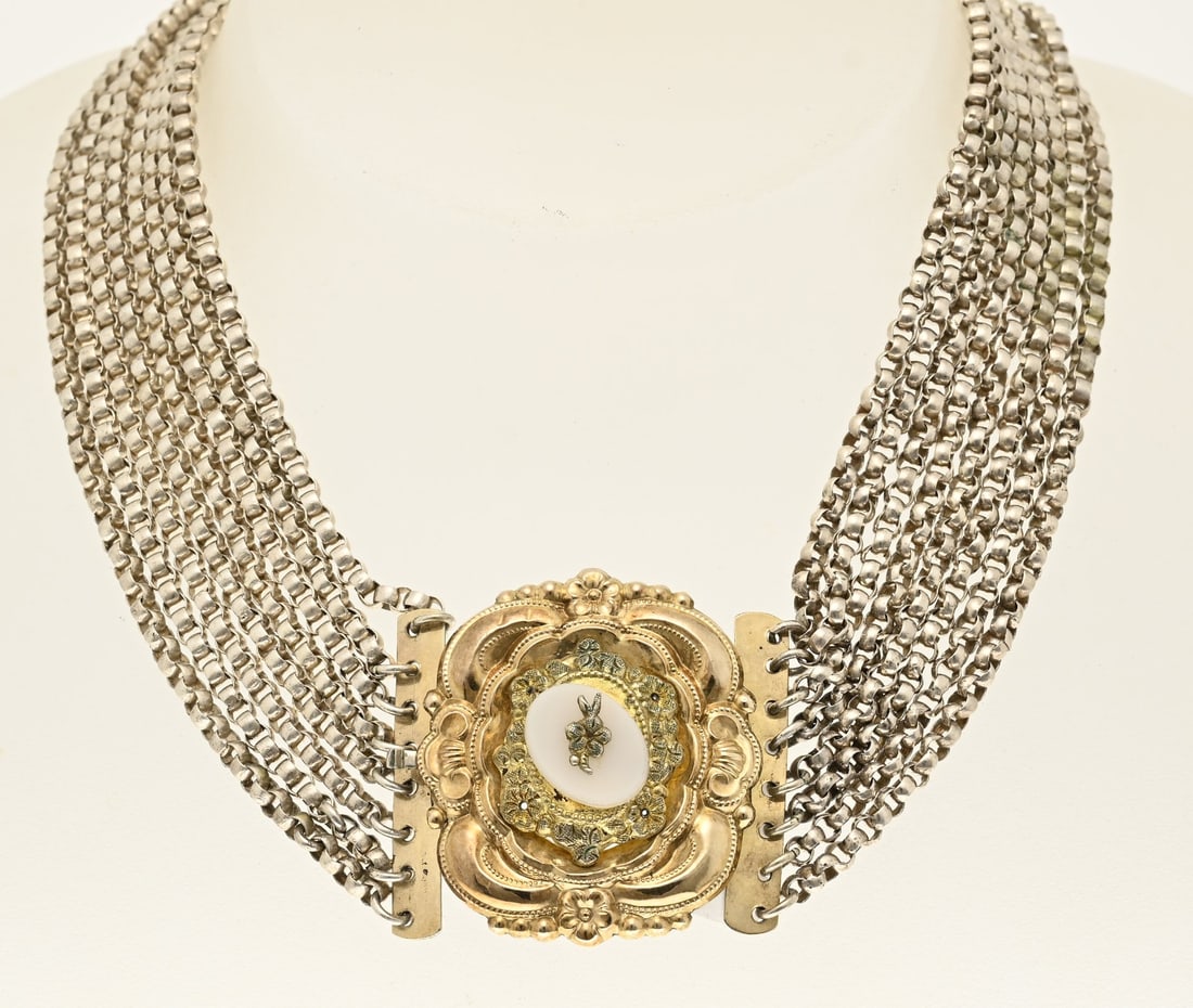 Silver choker with gold clasp: Silver choker with eight rows of jasseron links, attached to a gold and silver clasp. It is a rectangular, contoured design with twisted and floral decorations. The center is set with a white stone wi