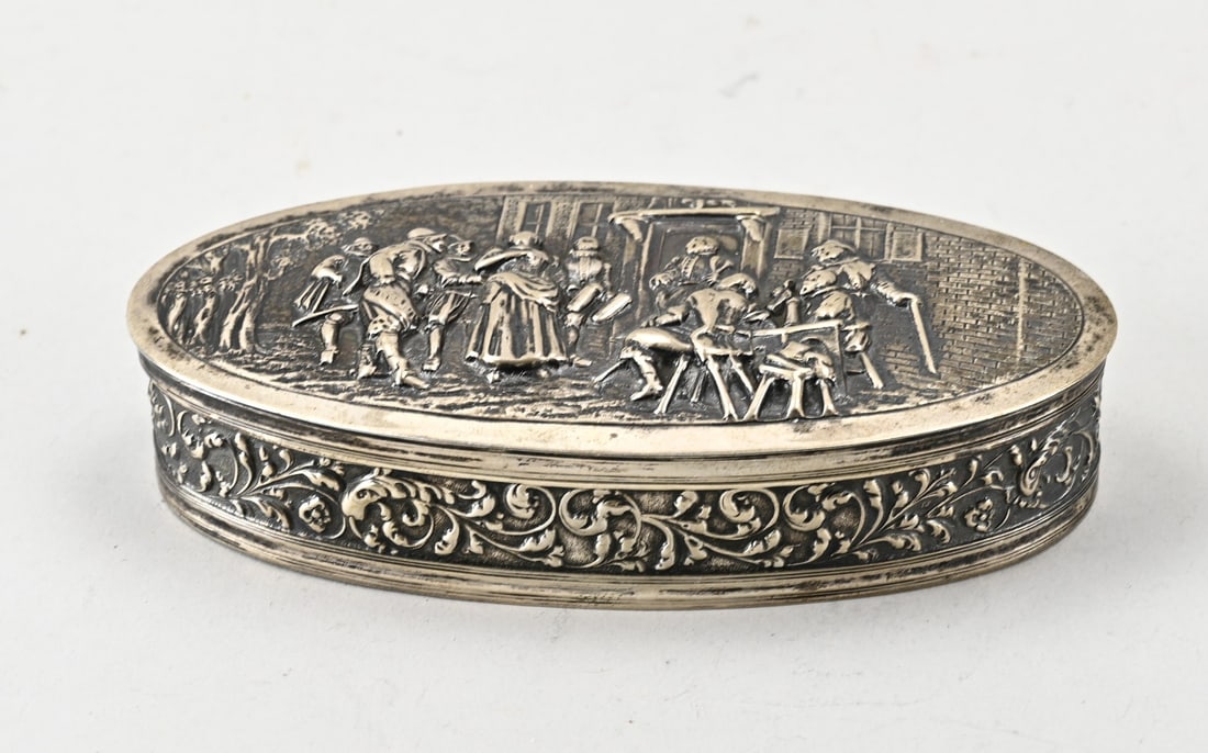 Silver box: Silver box, 833/000, oval model with a floral decorated rim and a hinged lid featuring a depiction with figures. MT.: Zaanlandse Zilversmederij, Amsterdam, dated:K:1920. 15x7.5x3cm. approx. 179 grams.