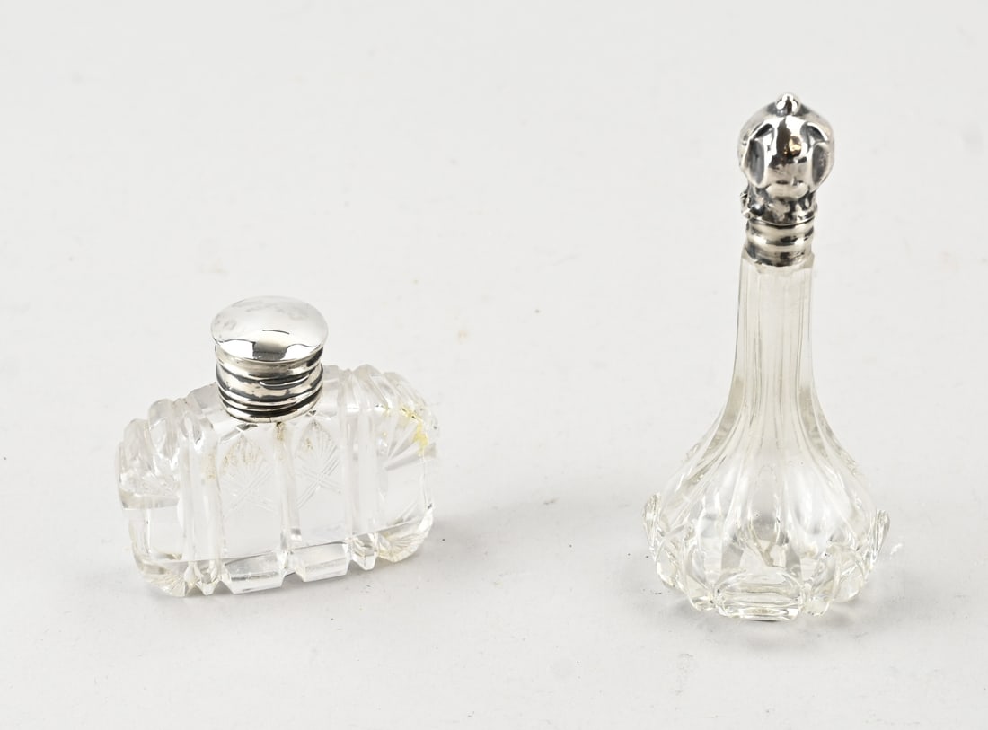 2 Crystal perfume bottles with silver: Two perfume bottles with silver. A long-necked bottle with cut glass and a silver collar and cap, 835/000, and a wide bottle with cut glass and a silver cap and collar, 925/000. Fitted with an inner