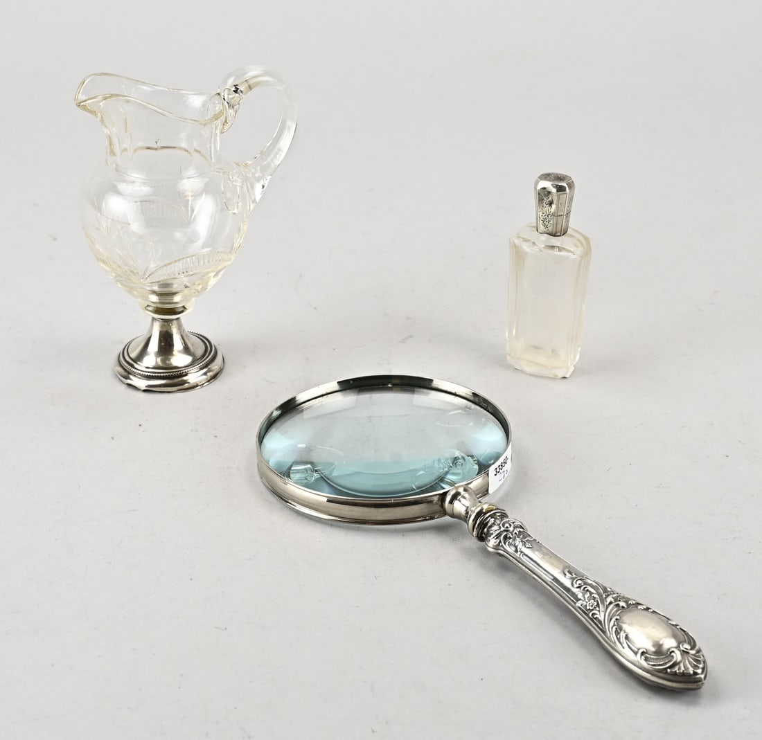 3 parts silver: Three pieces with silver, 835/000, perfume bottle with silver collar and cap, slightly dented, a crystal milk jug on a round silver base, and a magnifying glass with a silver handle with floral decora
