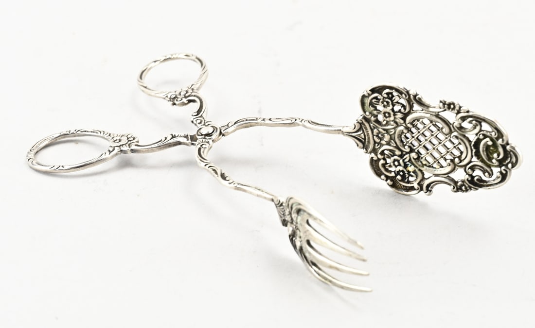 Silver pliers: Silver tongs, 800/000, with a sawed edge and a fork, attached to curved handles. The whole is decorated with floral motifs. Length 17 cm. Approx. 47 grams. Maker: Christoph Widmann, Pforzheim. In