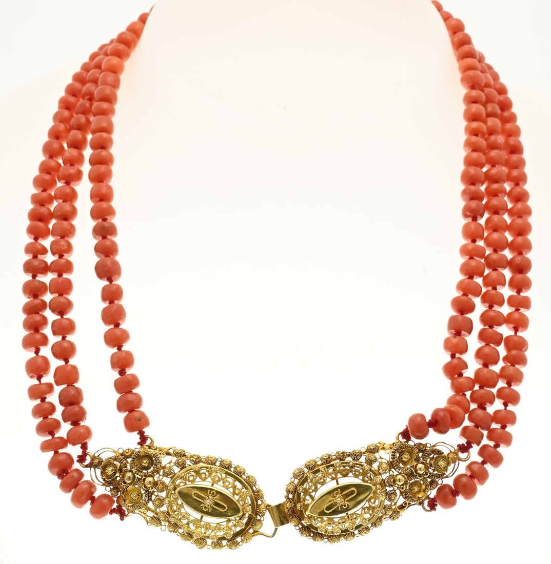 Blood coral necklace: Necklace of 3 rows of blood coral, barrel-shaped, ø 5.5 mm, attached to a yellow gold regional clasp, 585/000, with a hook, 2 pear-shaped sections decorated with buttons and filigree. Knotted. 42 cm,