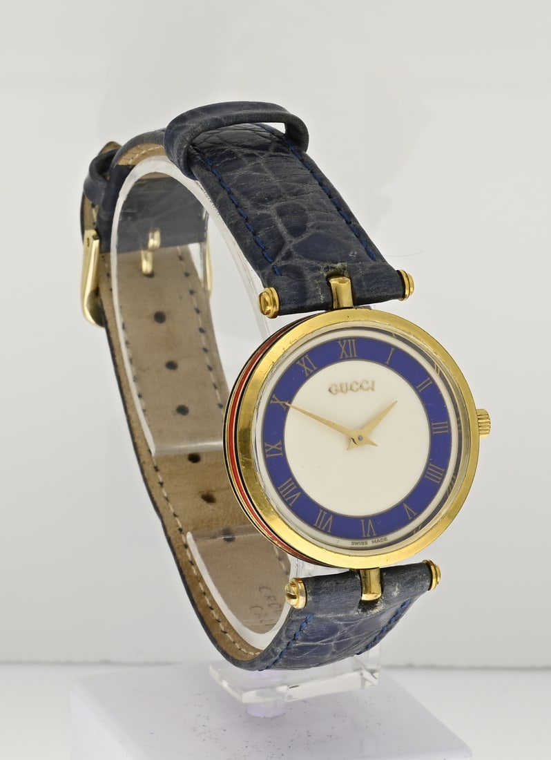 Gucci ladies' watch: Vintage Gucci watch, ladies' model, featuring a gold-plated round case, ø 30 mm, with red and blue enamel lines on the case bezel. A cream-colored dial with a blue rim. Fitted with a blue strap. Show